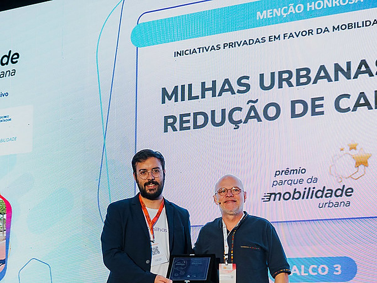 Lucas Nicoleti recebendo a Menção Honrosa no palco do Prêmio PMU, com o case Milhas Urbanas no telão